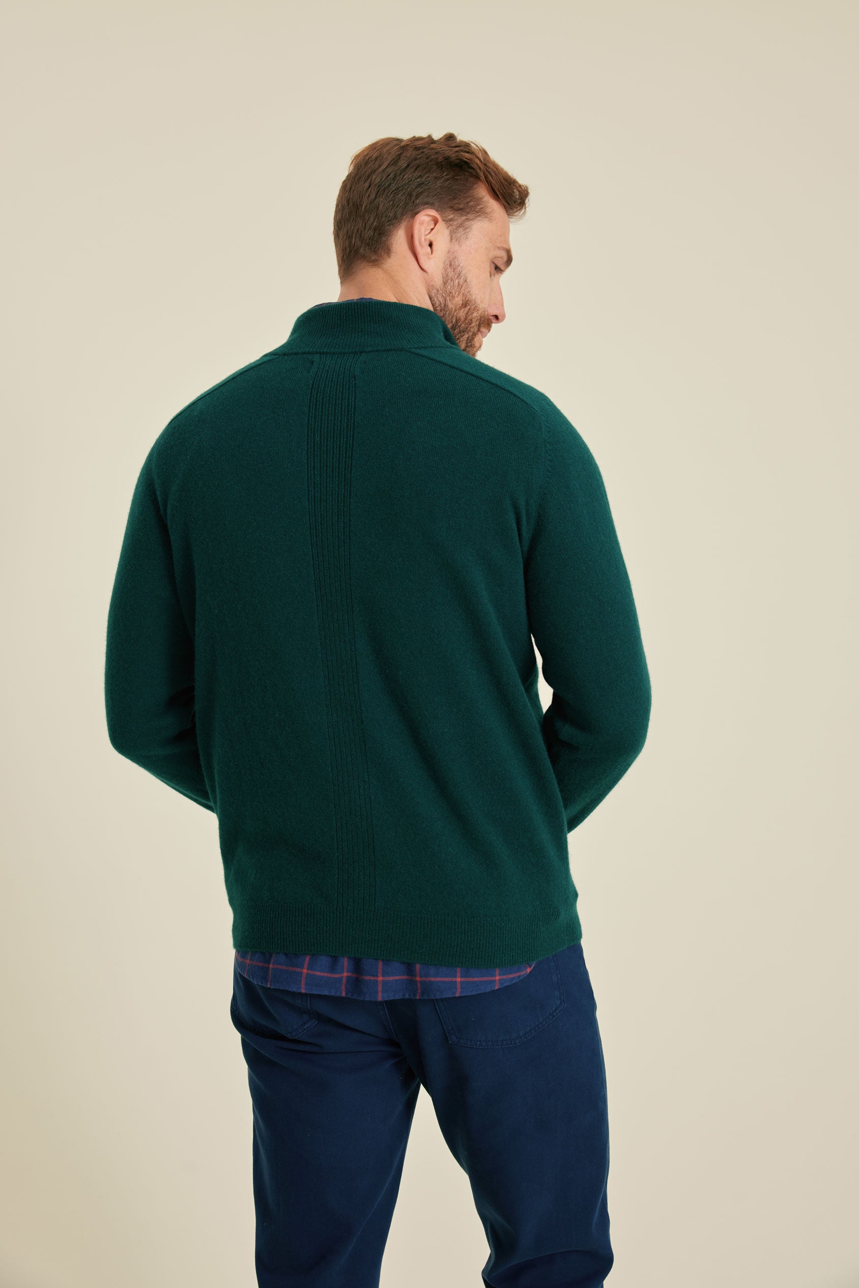Man wearing a green sweater and blue pants on a beige background