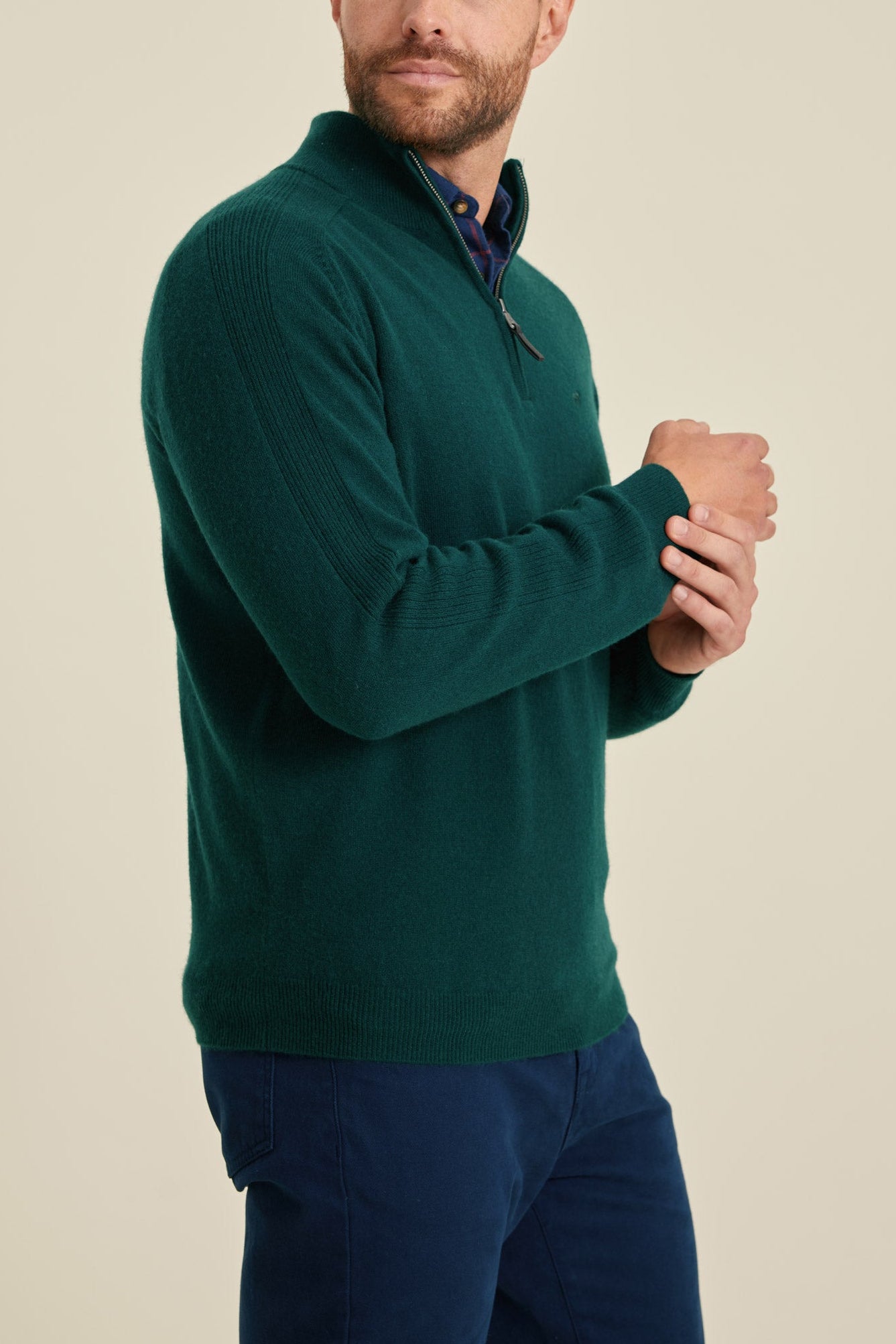 Man wearing a green sweater and blue pants against a beige background