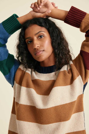 Woman wearing a striped sweater with two people holding hands above her head.