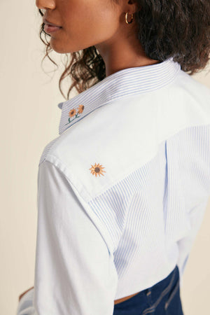 Close-up of a person wearing a white shirt with embroidered designs on a beige background