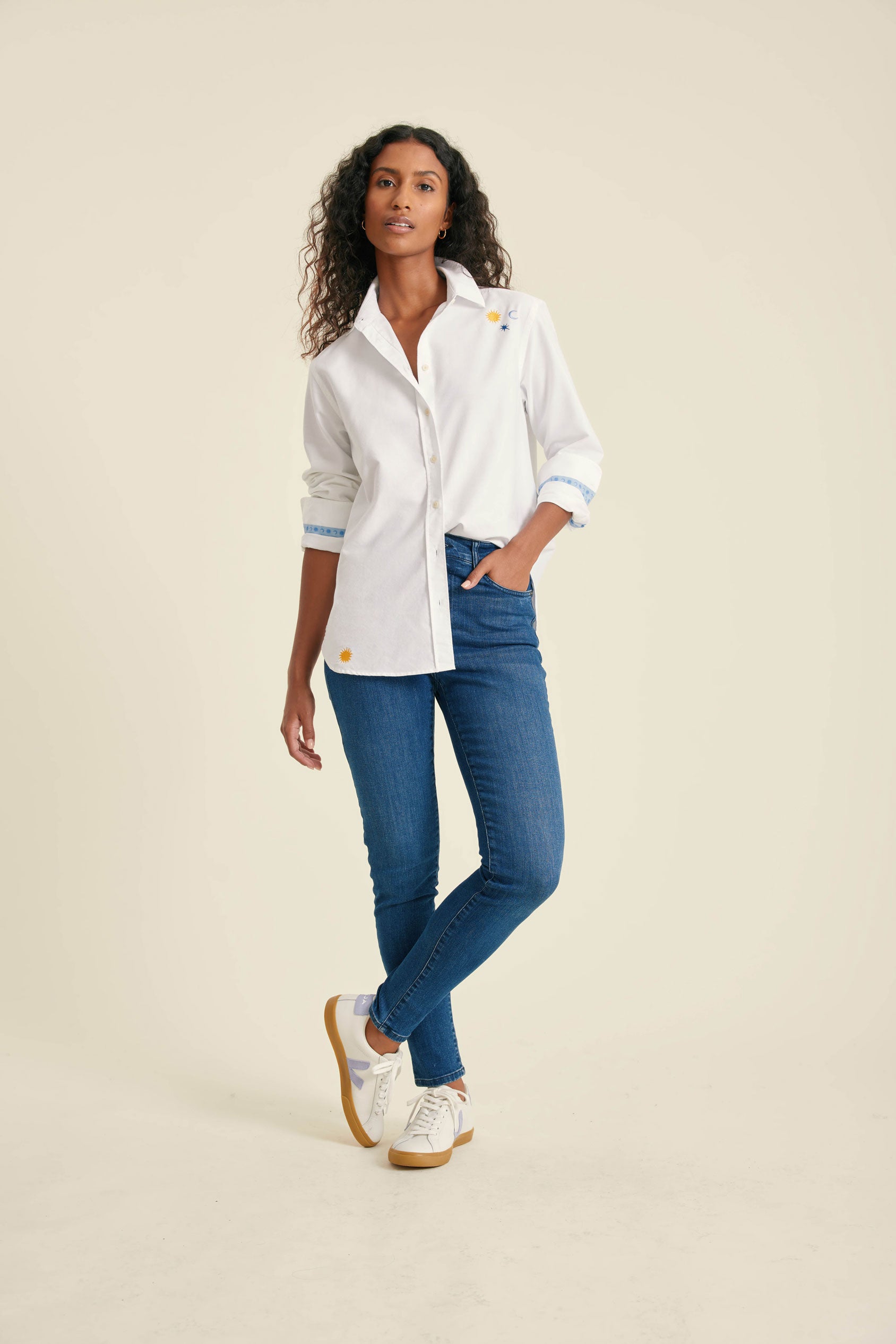 Woman wearing a white shirt, blue jeans, and white sneakers on a beige background