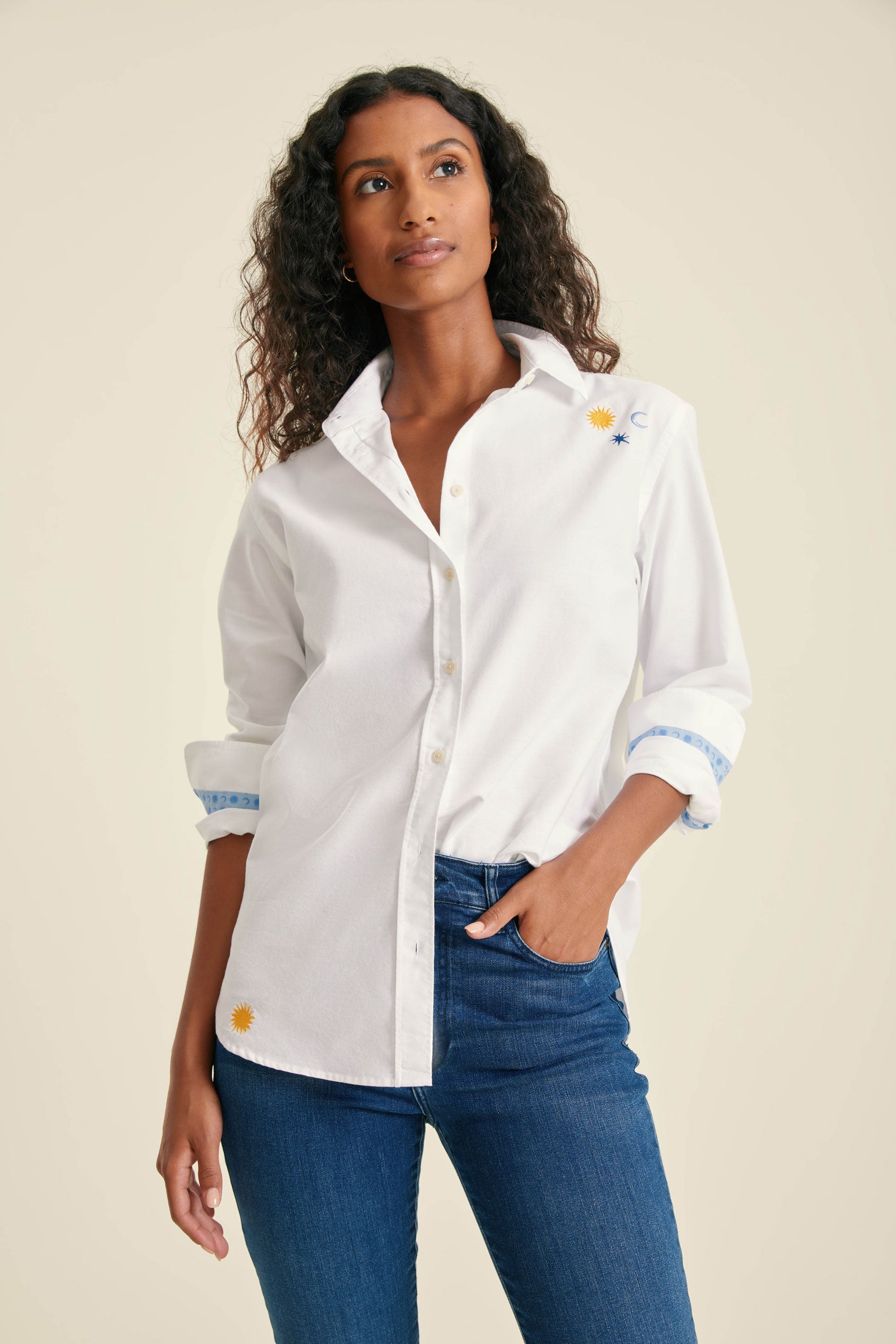 Woman wearing a white shirt with rolled-up sleeves and blue jeans on a beige background