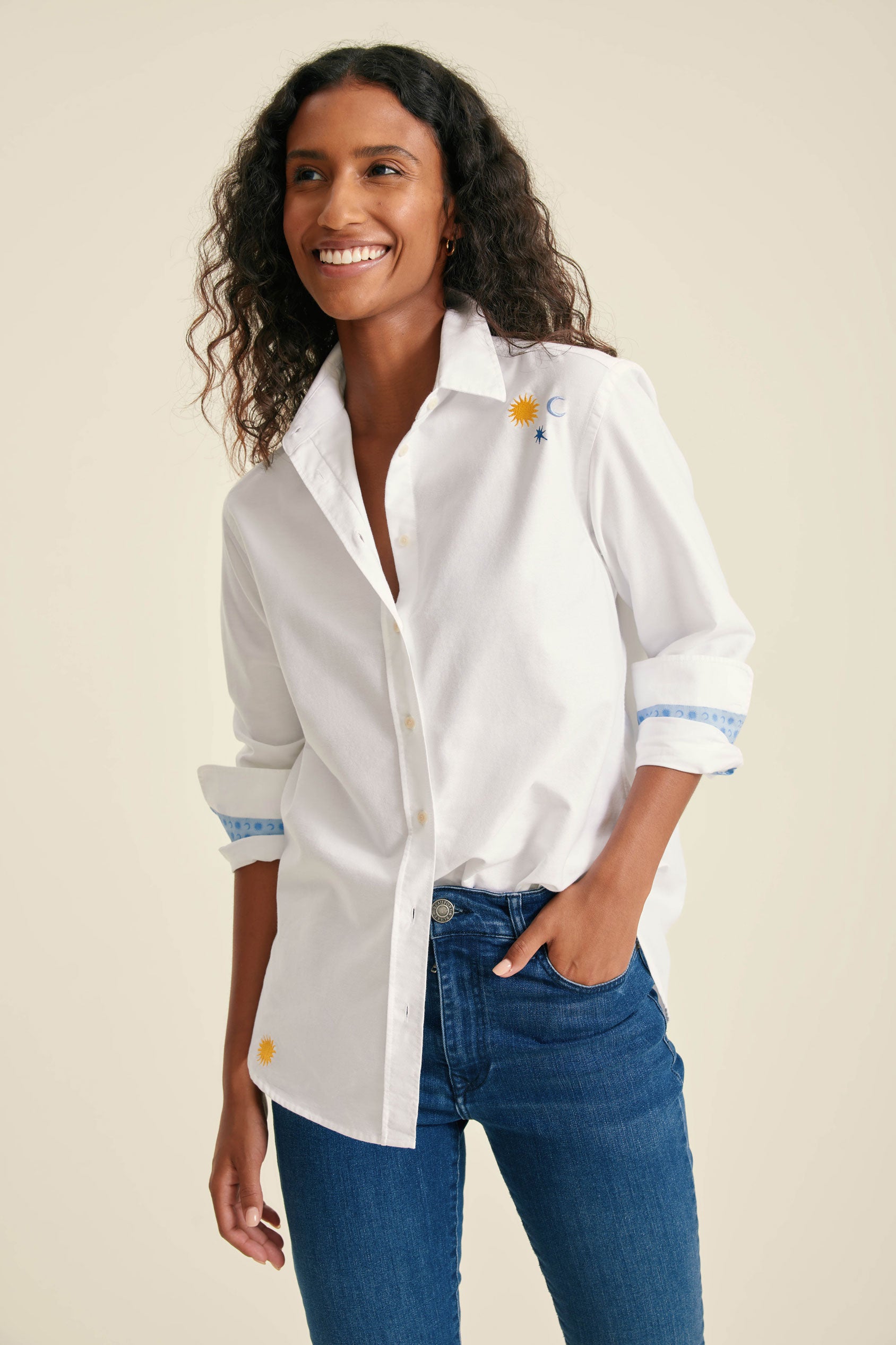 Woman wearing a white button-up shirt with blue accents and jeans on a beige background