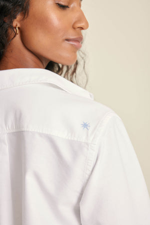 White shirt with a small embroidered design on the chest, worn by a person.