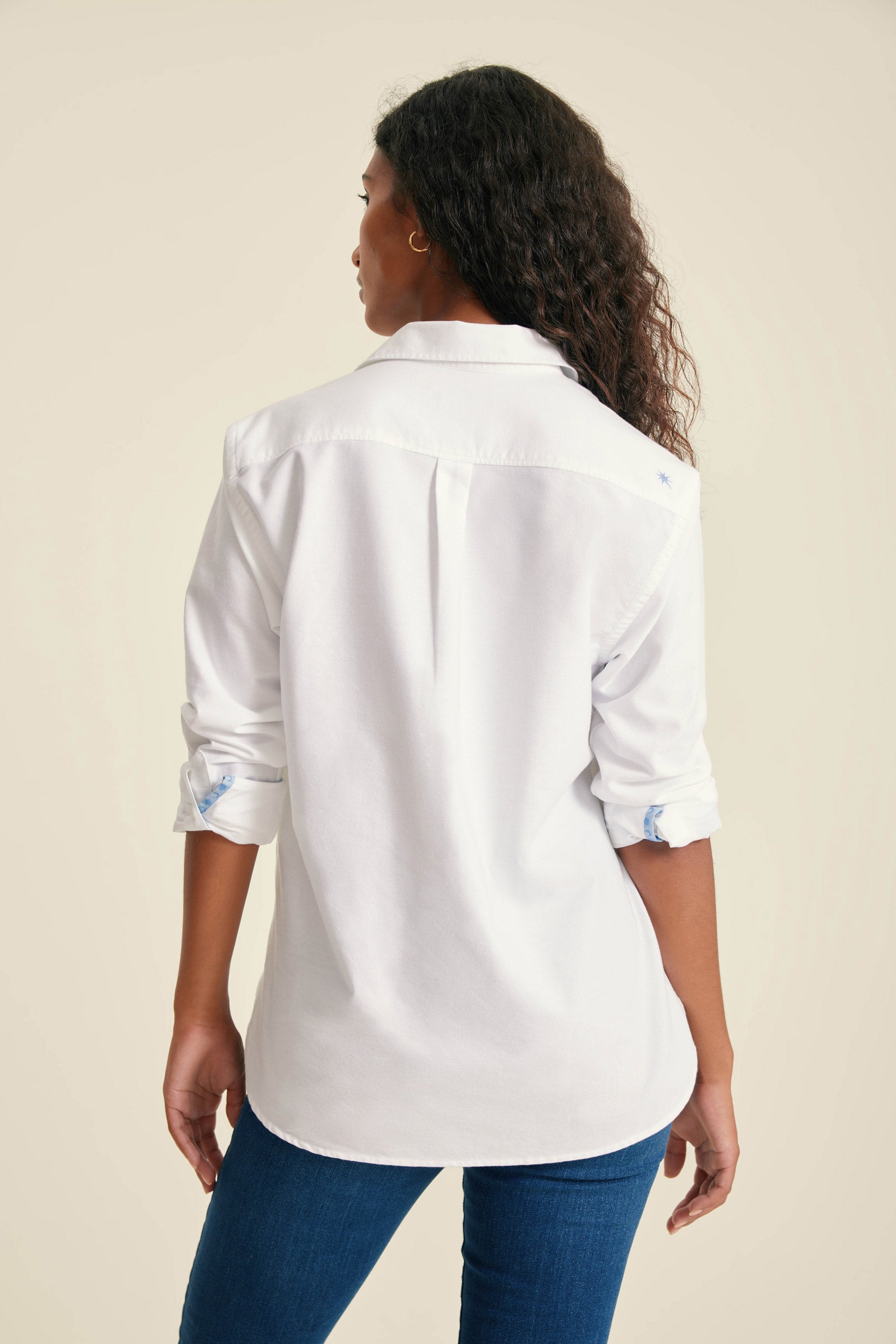 Person wearing a white shirt with rolled-up sleeves on a beige background