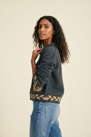 Woman wearing a dark gray sweater with patterned sleeves against a beige background
