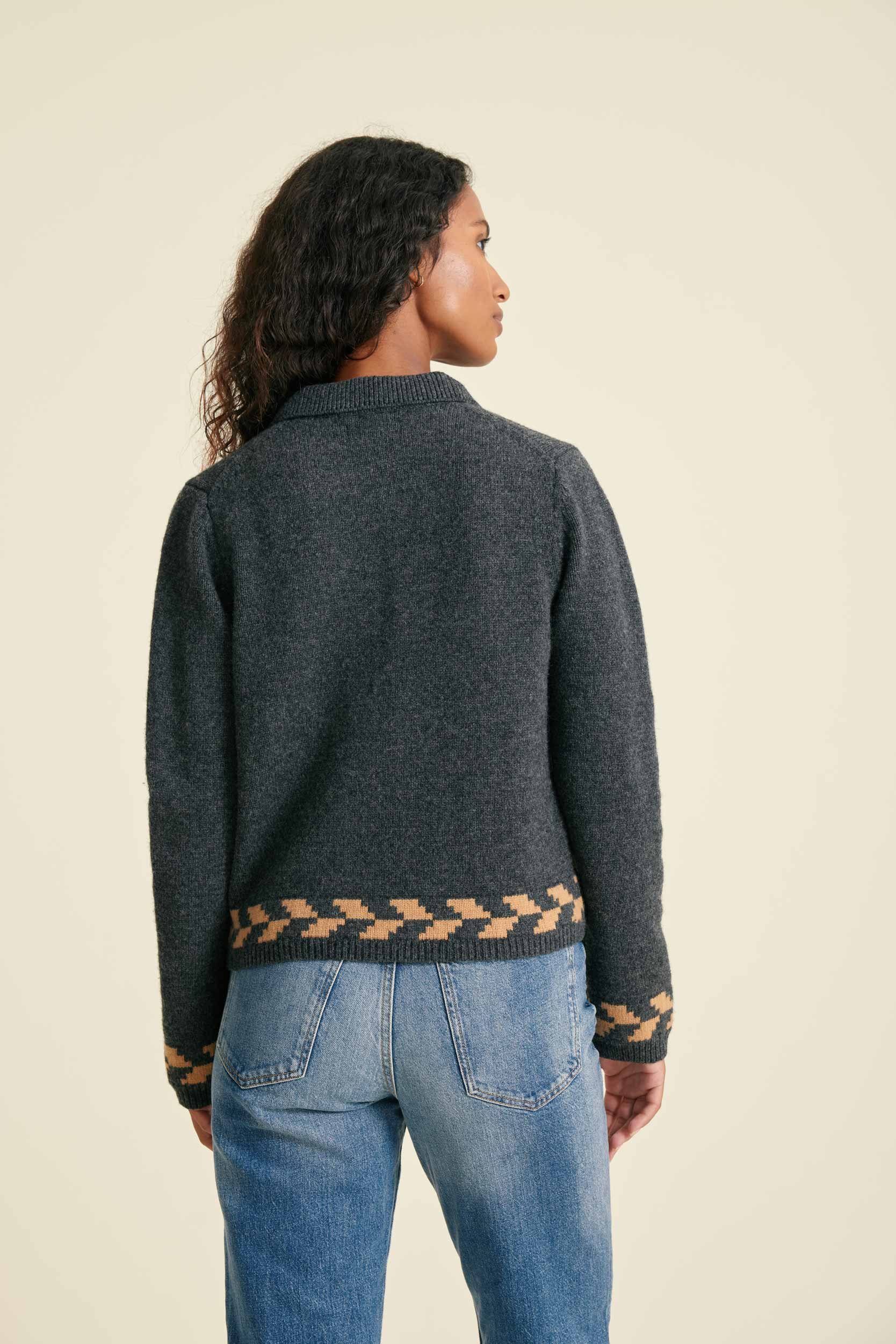 Person wearing a dark gray sweater with patterned hem on a beige background