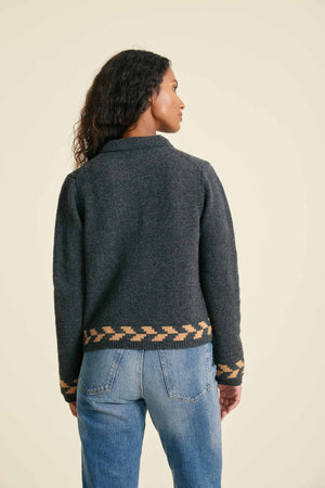 Person wearing a dark gray sweater with patterned hem on a beige background