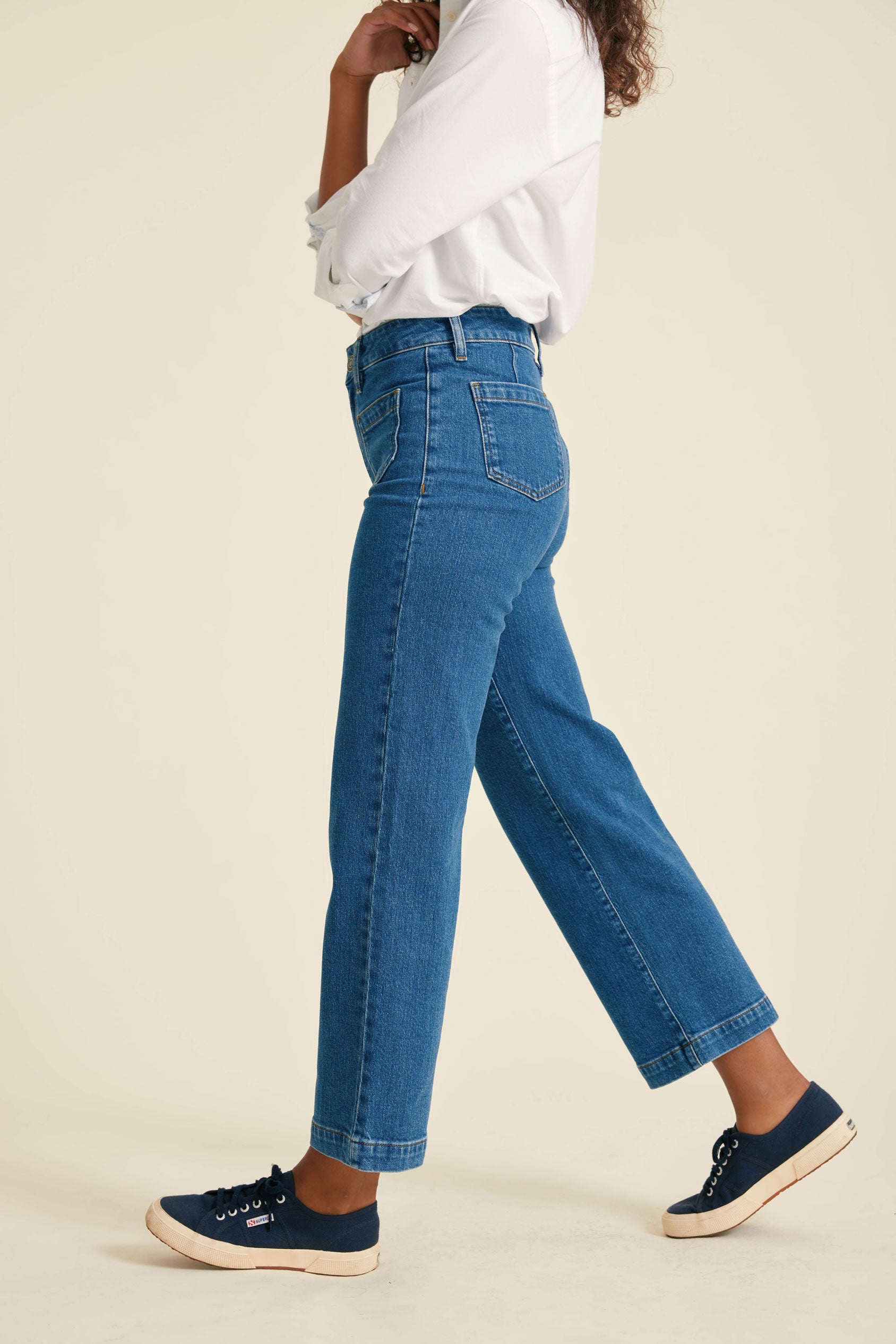 Person wearing blue jeans and navy sneakers on a beige background