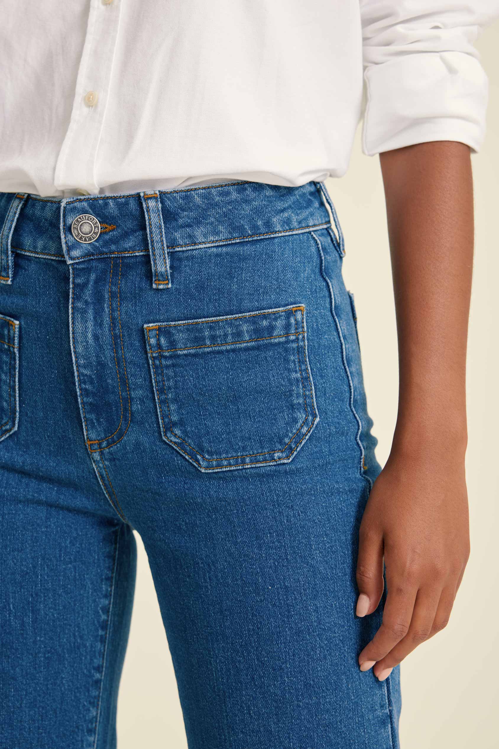Close-up of blue jeans with a white shirt underneath on a beige background