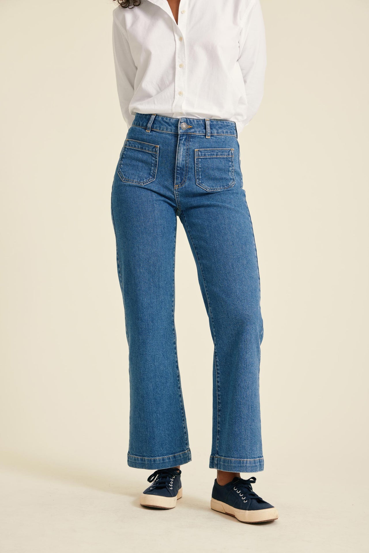 Person wearing blue jeans and a white shirt on a beige background