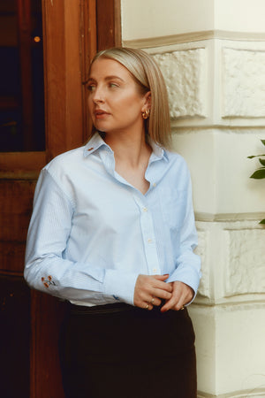 Woman wearing a light blue shirt standing in front of a building entrance.