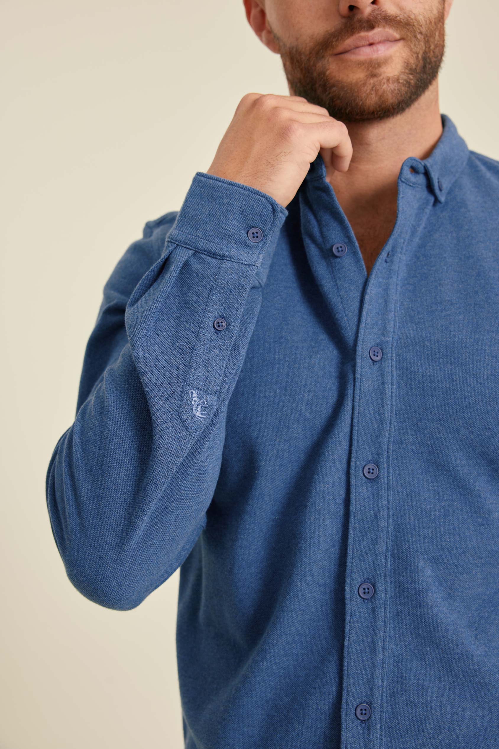 Man wearing a blue button-up shirt against a beige background