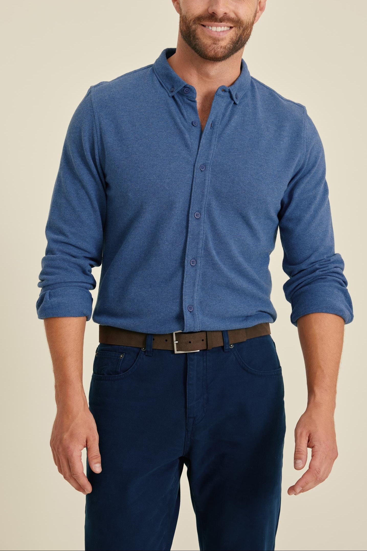 Man wearing a blue shirt and dark pants against a beige background