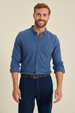 Man wearing a blue shirt and dark pants against a beige background