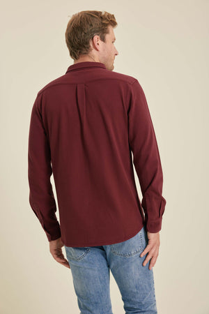 Man wearing a burgundy shirt and blue jeans on a beige background