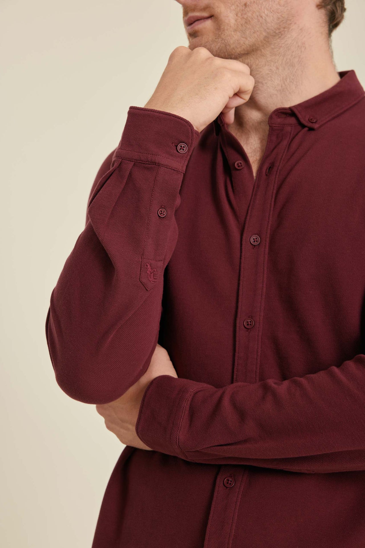 Man wearing a burgundy shirt with rolled-up sleeves against a beige background
