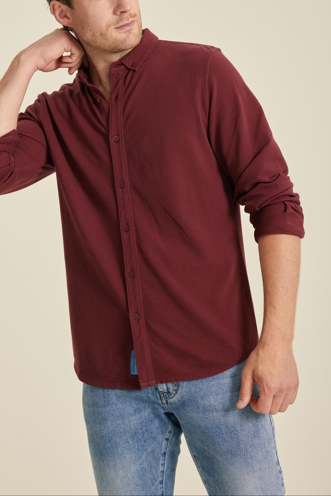 Man wearing a burgundy shirt and blue jeans against a beige background
