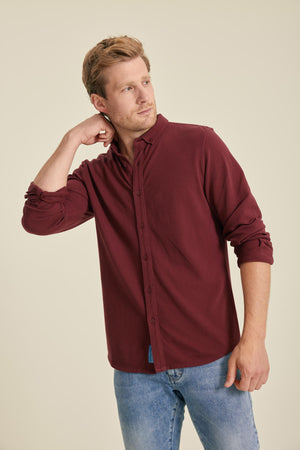Man wearing a burgundy shirt and blue jeans against a beige background