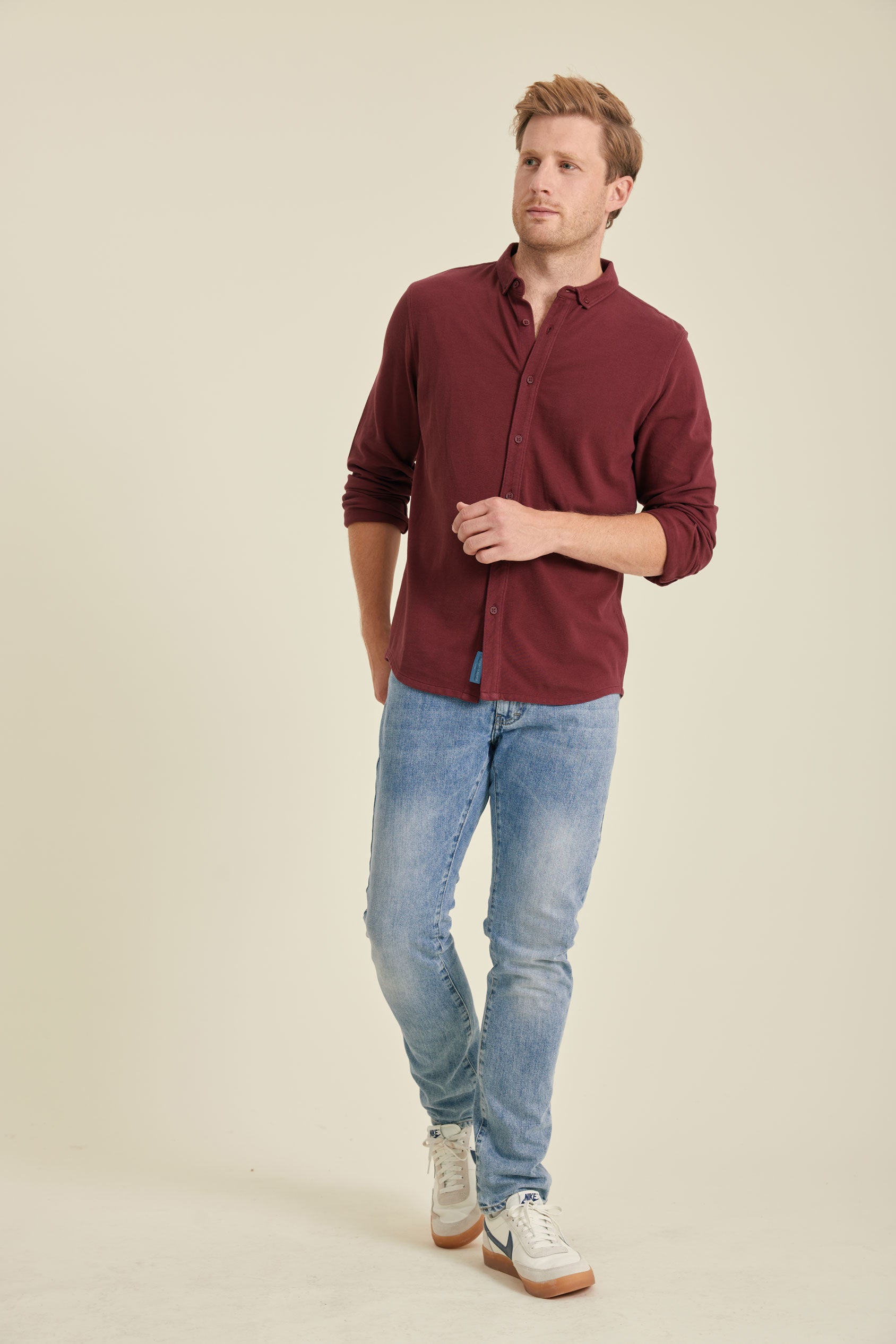 Man wearing a burgundy shirt and light blue jeans on a beige background