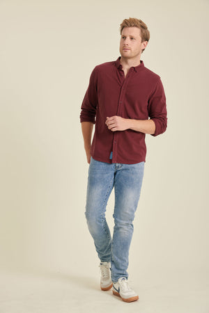 Man wearing a burgundy shirt and light blue jeans on a beige background