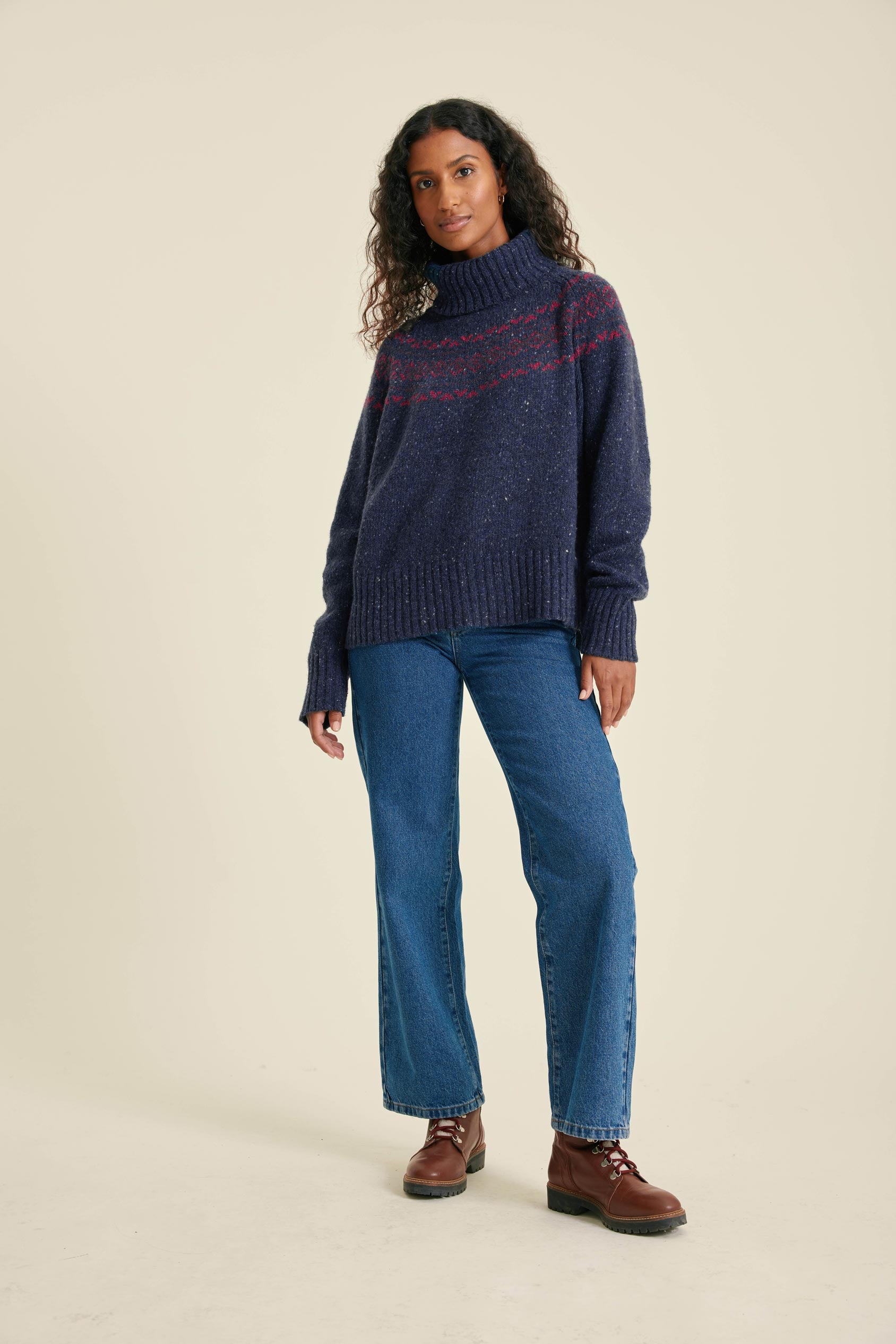Woman wearing a blue sweater with red accents and blue jeans on a beige background
