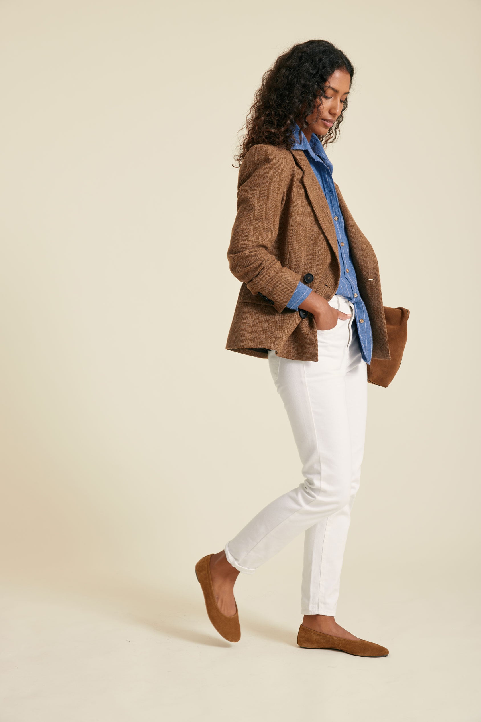 Woman wearing a brown blazer, white pants, and brown shoes on a beige background