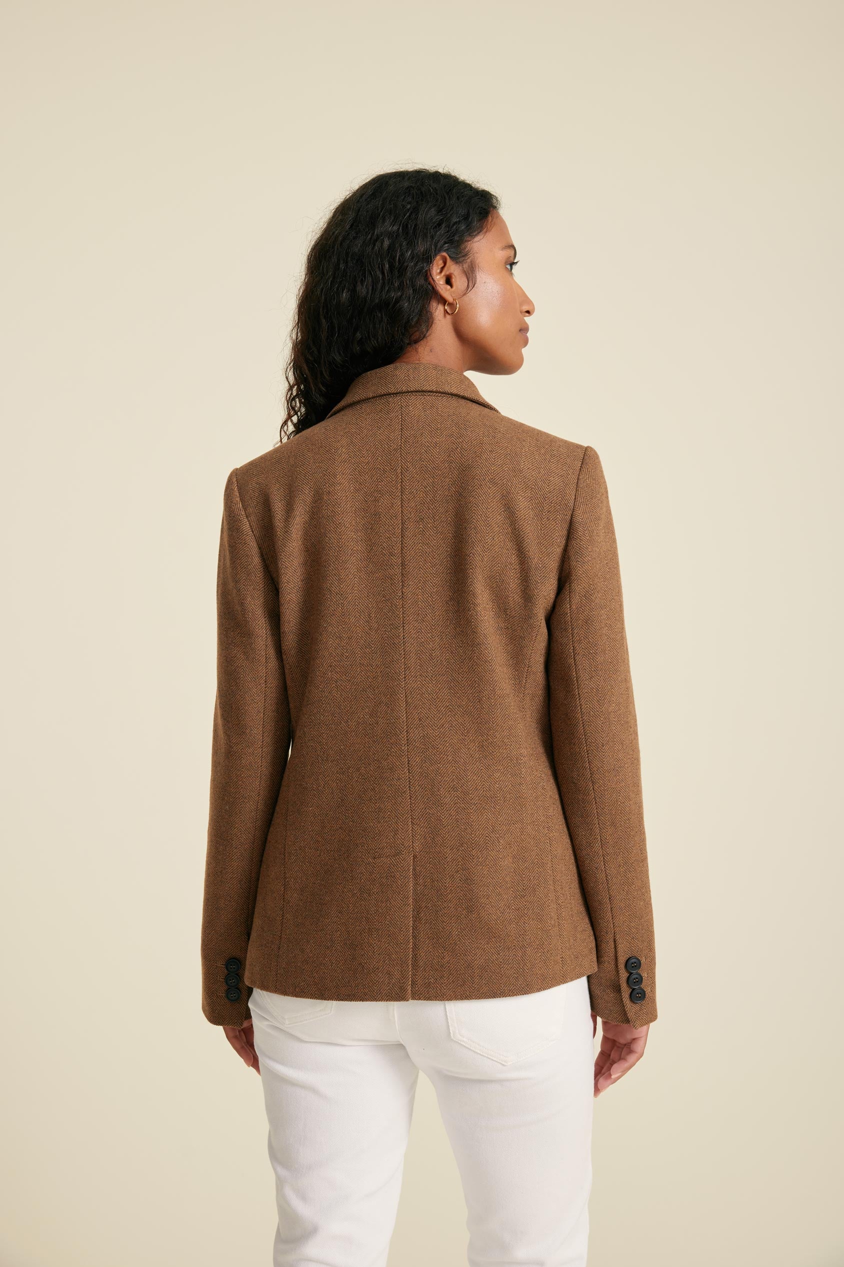 Woman wearing a brown jacket and white pants on a beige background