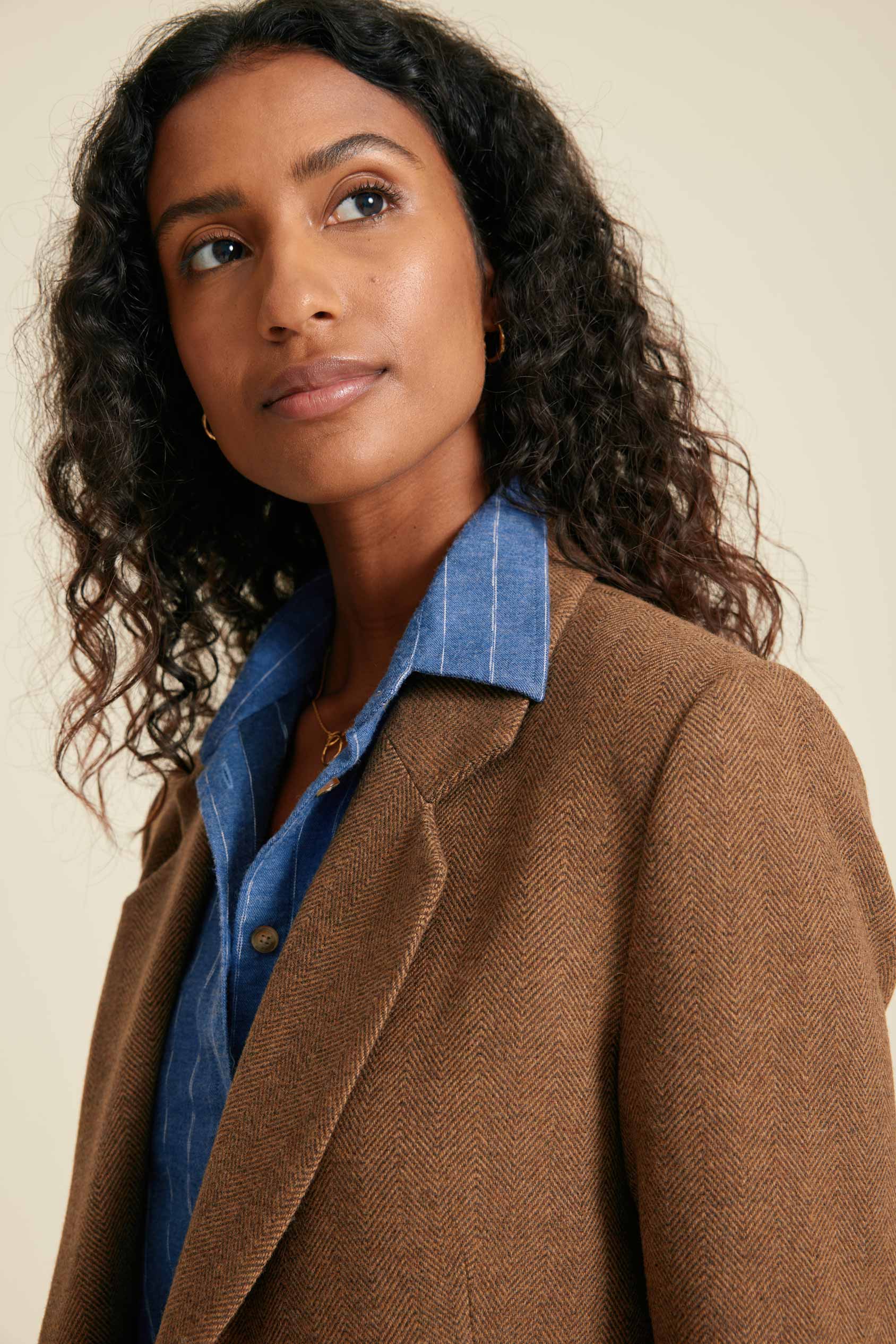 Woman wearing a brown coat over a blue shirt against a beige background