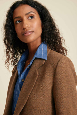 Woman wearing a brown coat over a blue shirt against a beige background