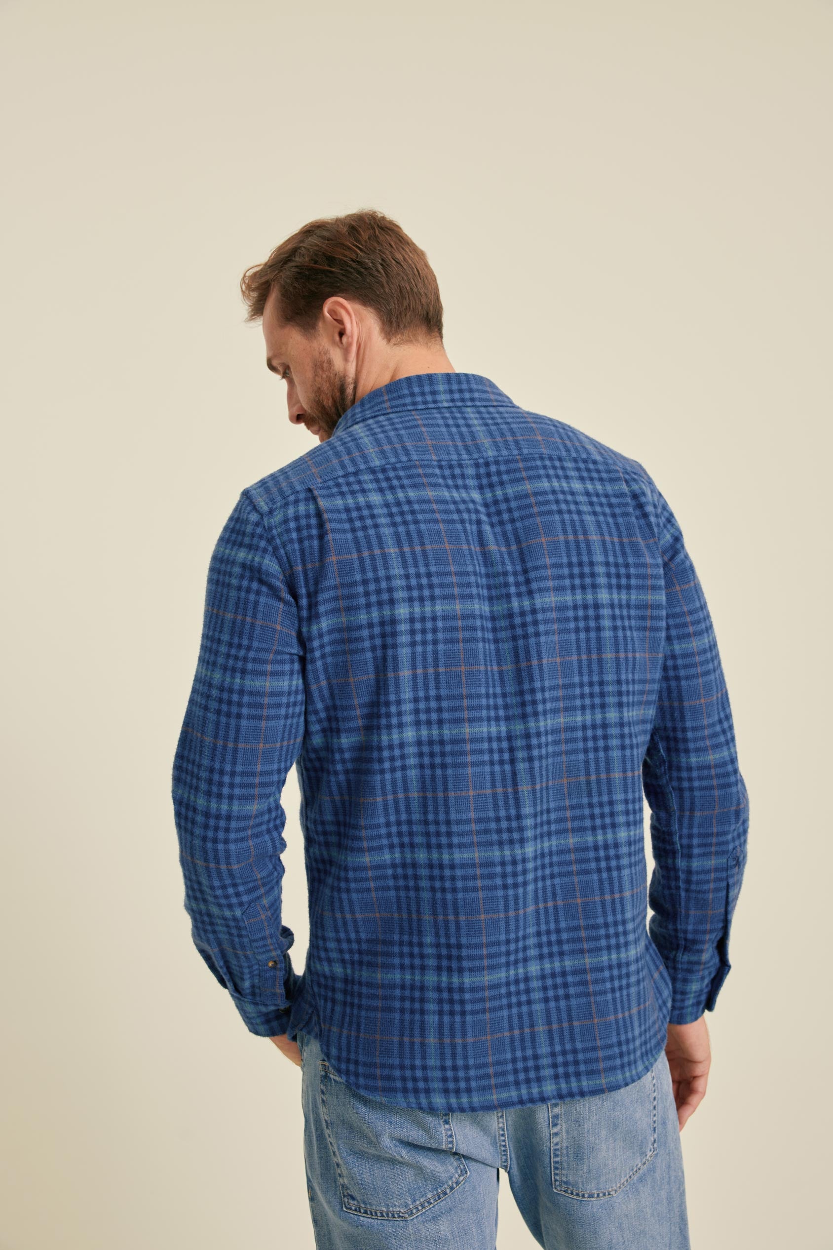 Man wearing a blue plaid shirt against a beige background