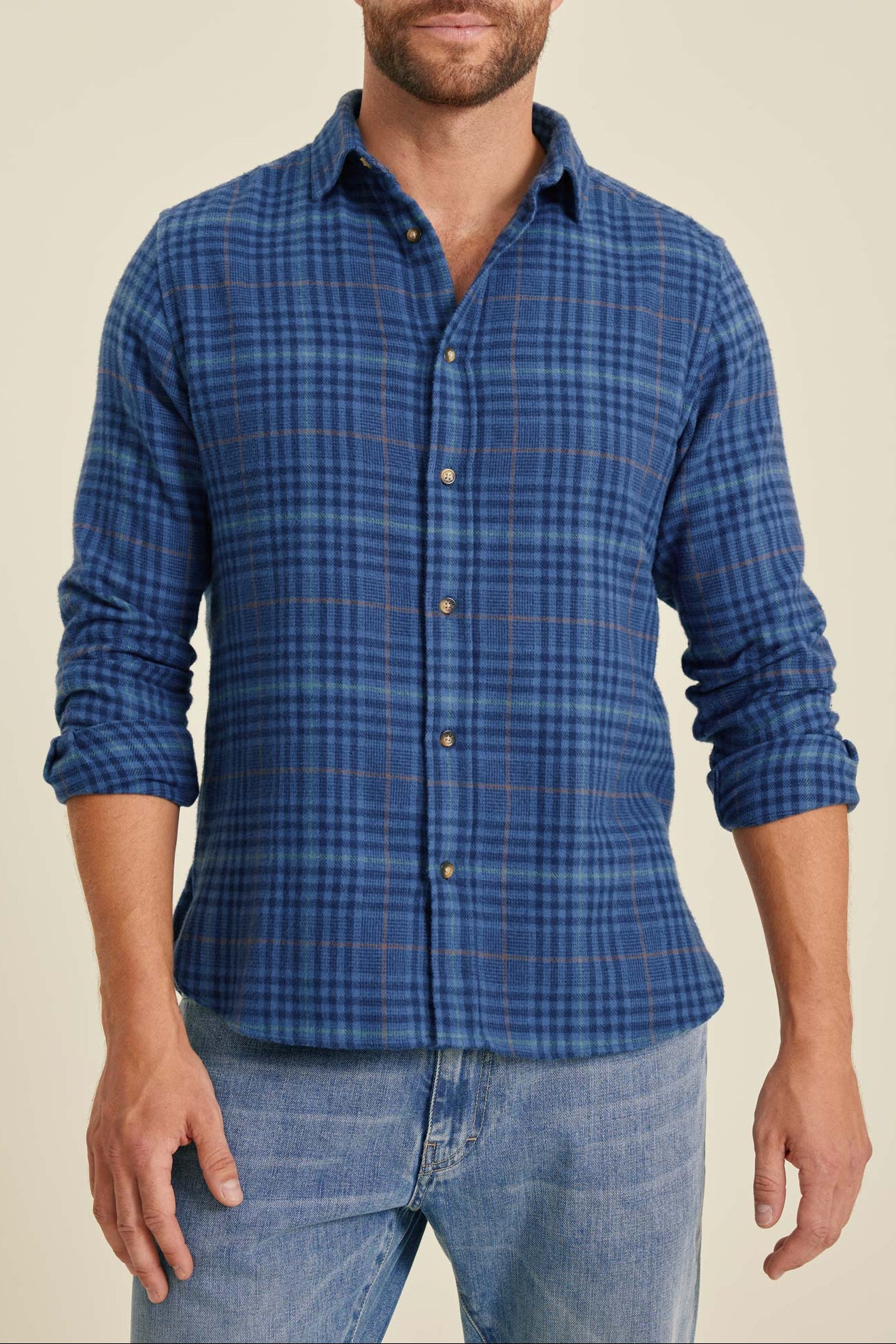 Man wearing a blue plaid shirt and jeans on a beige background