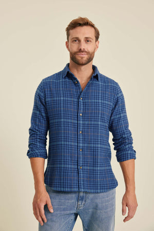 Man wearing a blue plaid shirt and jeans on a beige background