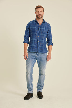 Man wearing a blue checkered shirt and light blue jeans on a beige background