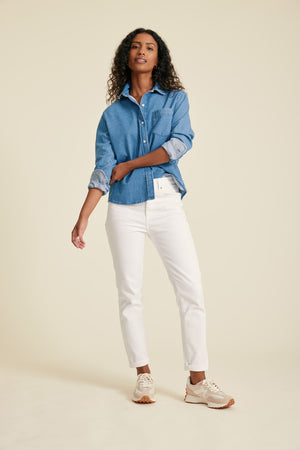 Woman wearing a blue denim shirt and white pants on a beige background