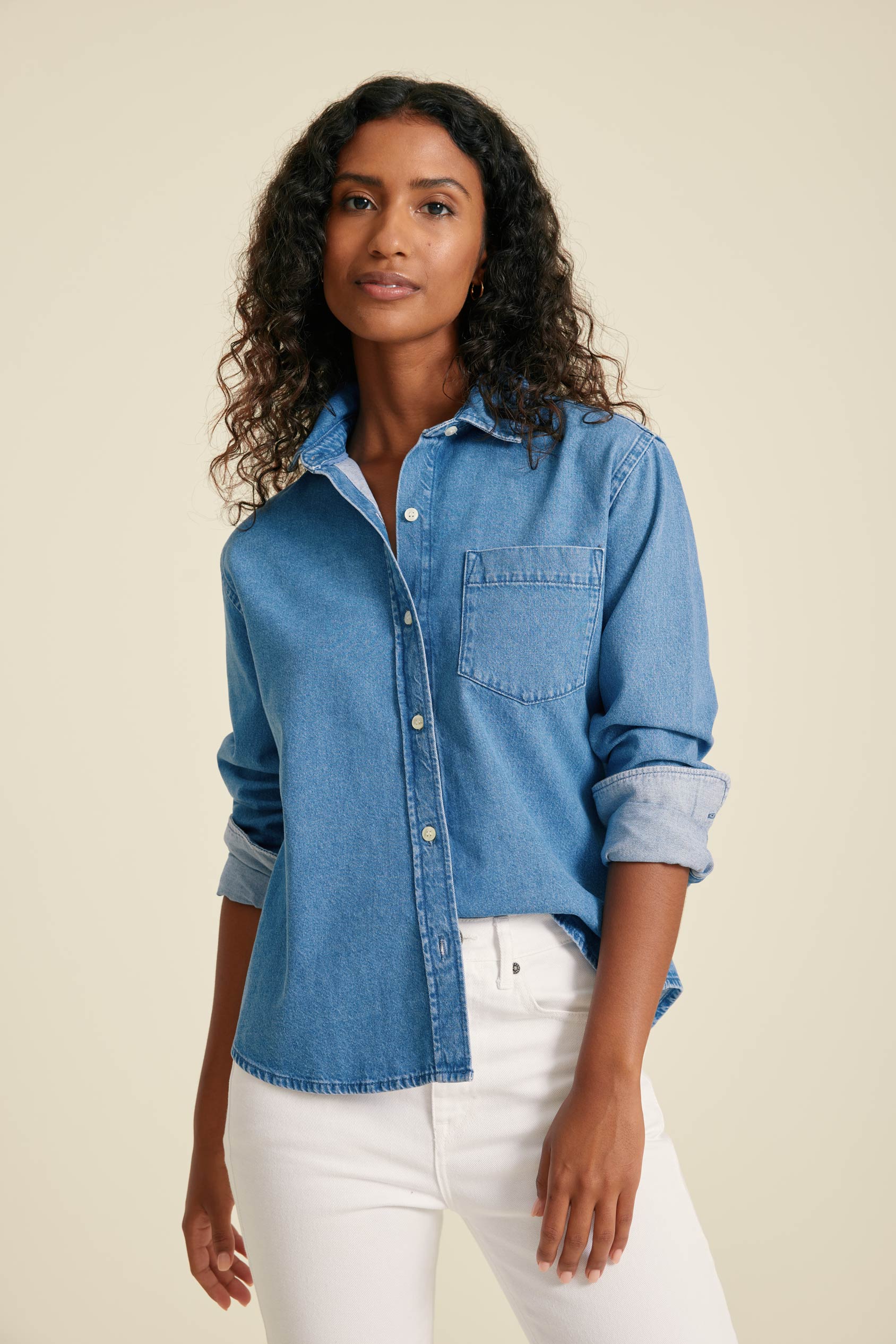 Woman wearing a blue denim shirt and white pants against a beige background