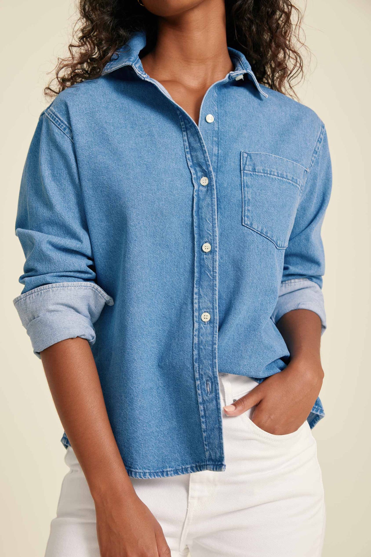 Person wearing a blue denim shirt with rolled-up sleeves on a beige background