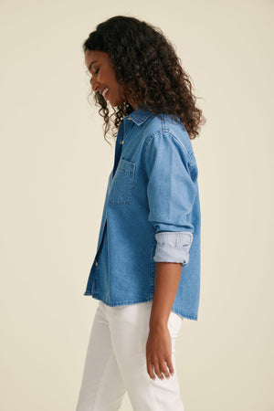 Woman wearing a blue denim shirt and white pants on a beige background