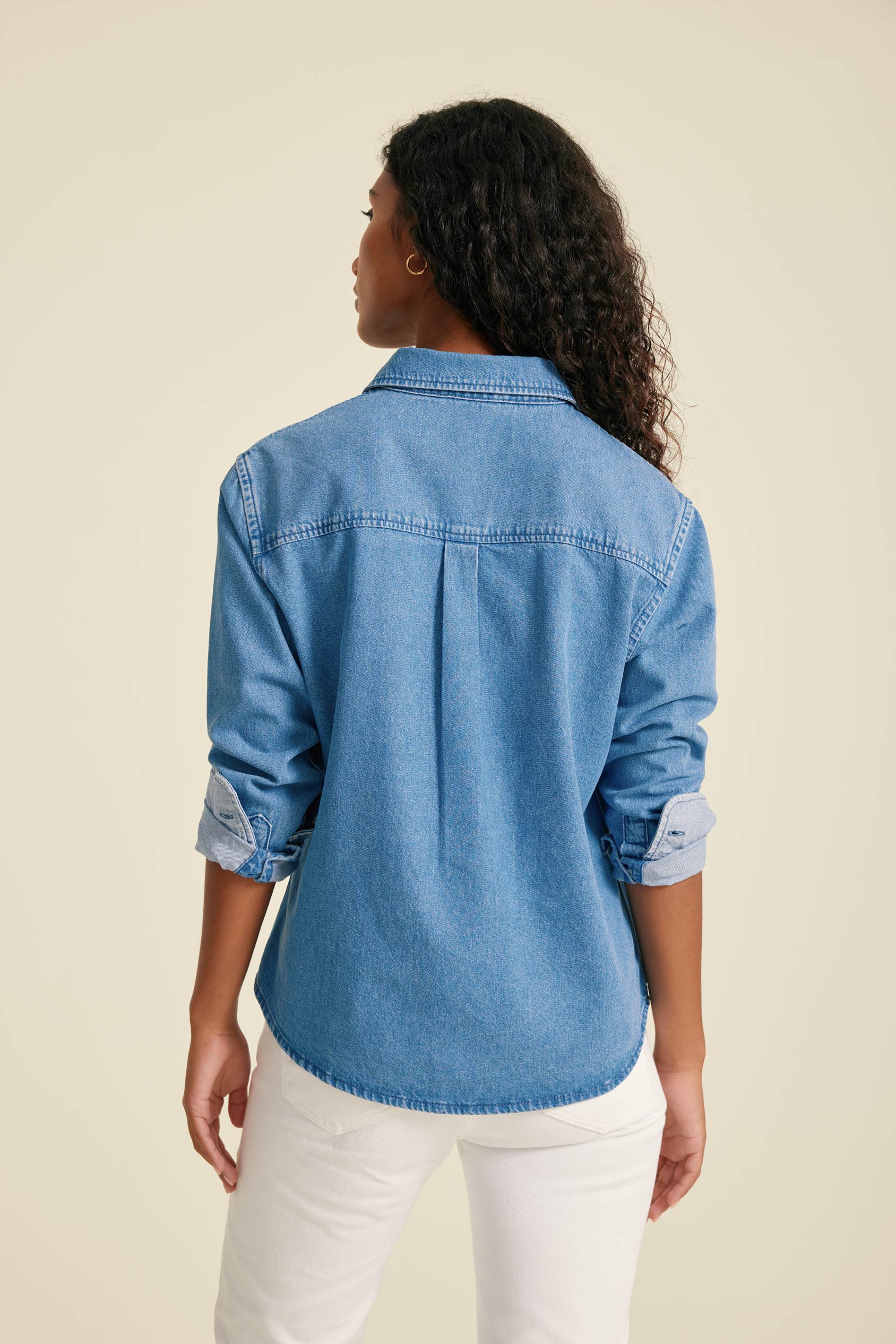 Woman wearing a blue denim shirt and white pants against a beige background