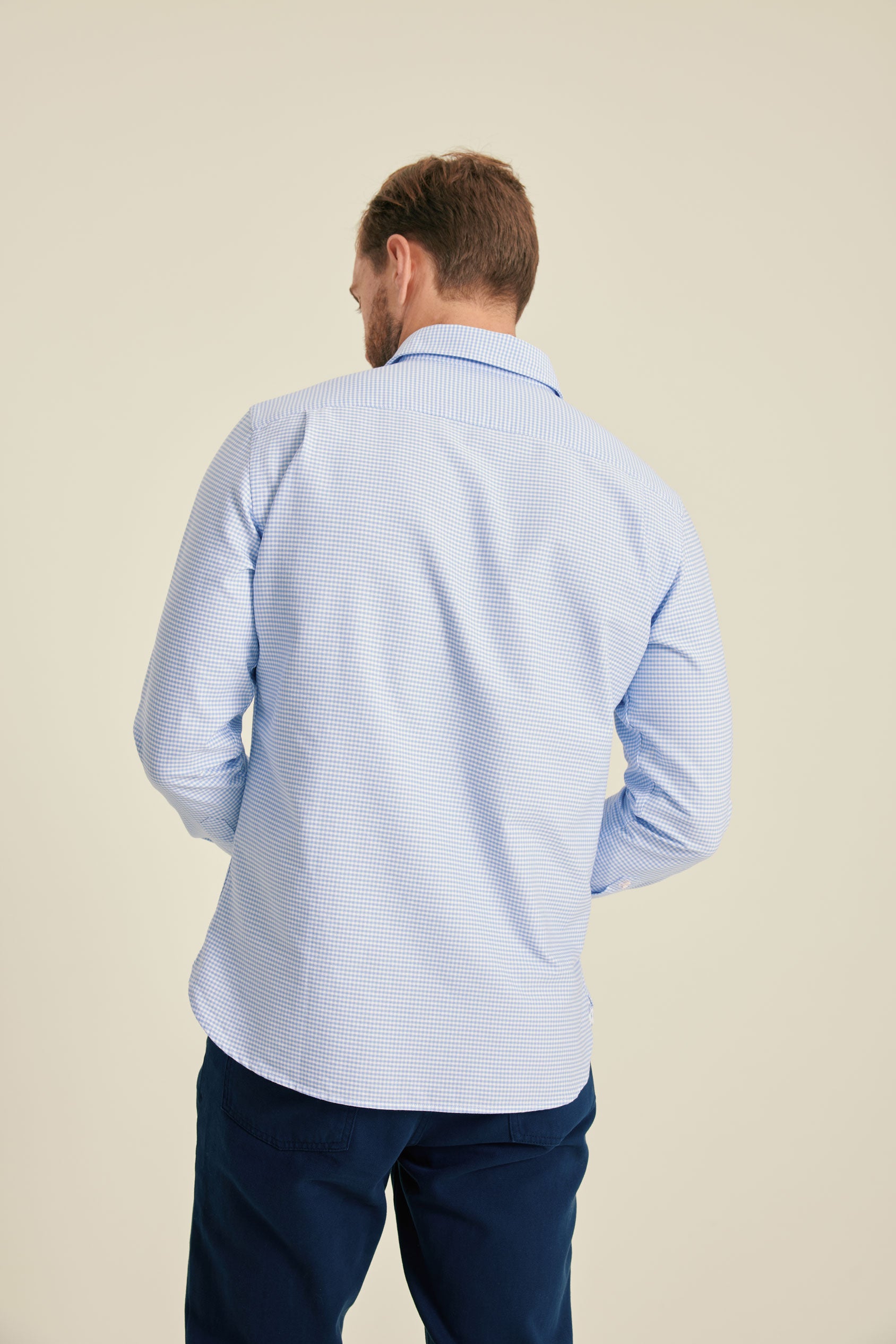 Man wearing a light blue checkered shirt and dark blue pants on a beige background