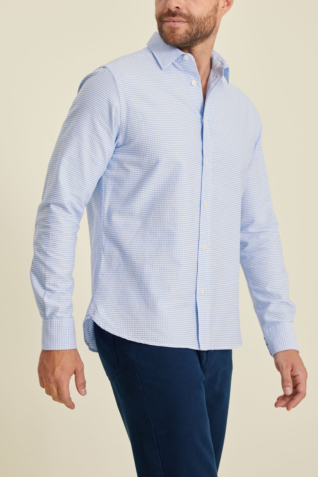Man wearing a light blue checkered shirt and dark blue pants on a beige background