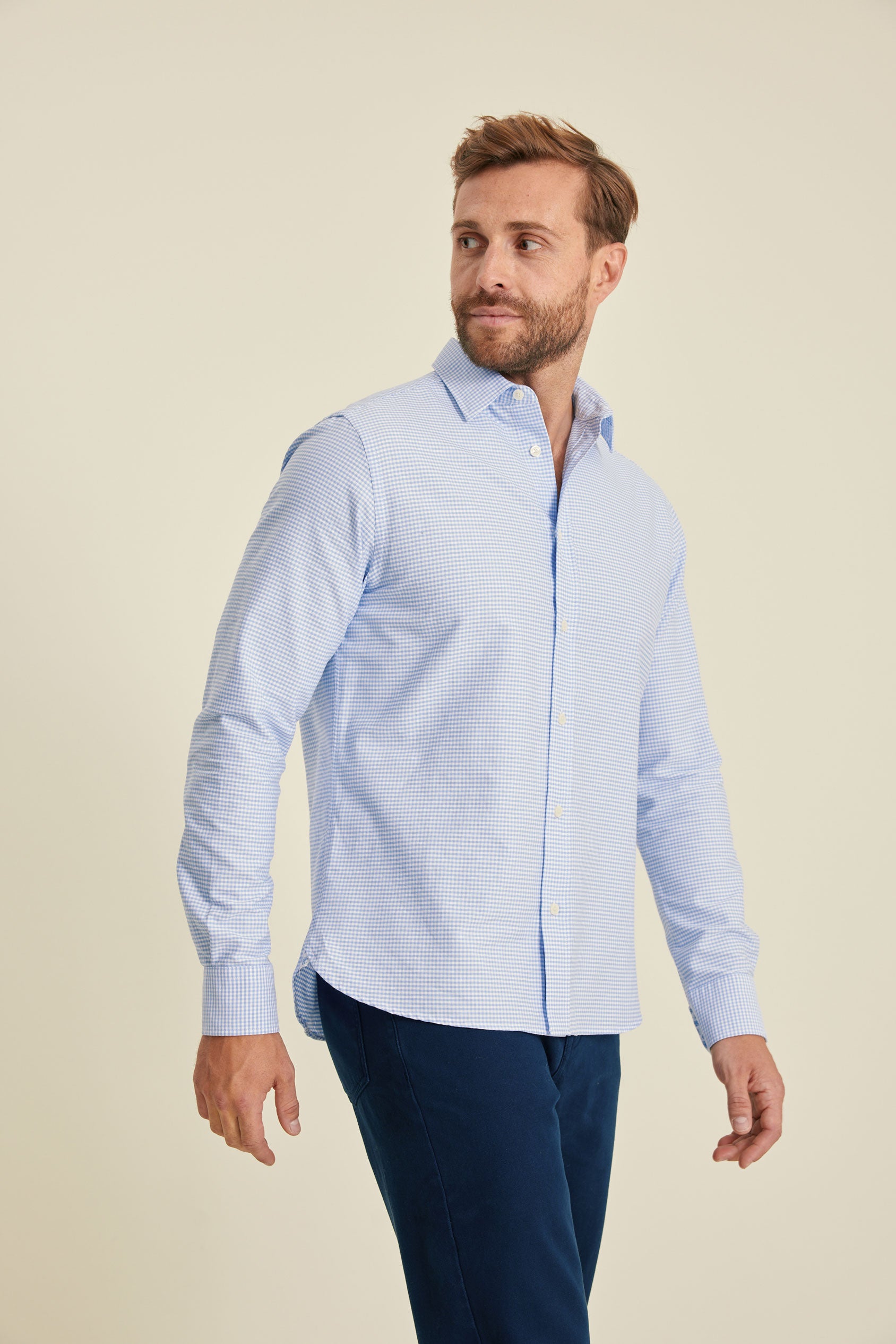 Man wearing a light blue checkered shirt and dark blue pants on a beige background
