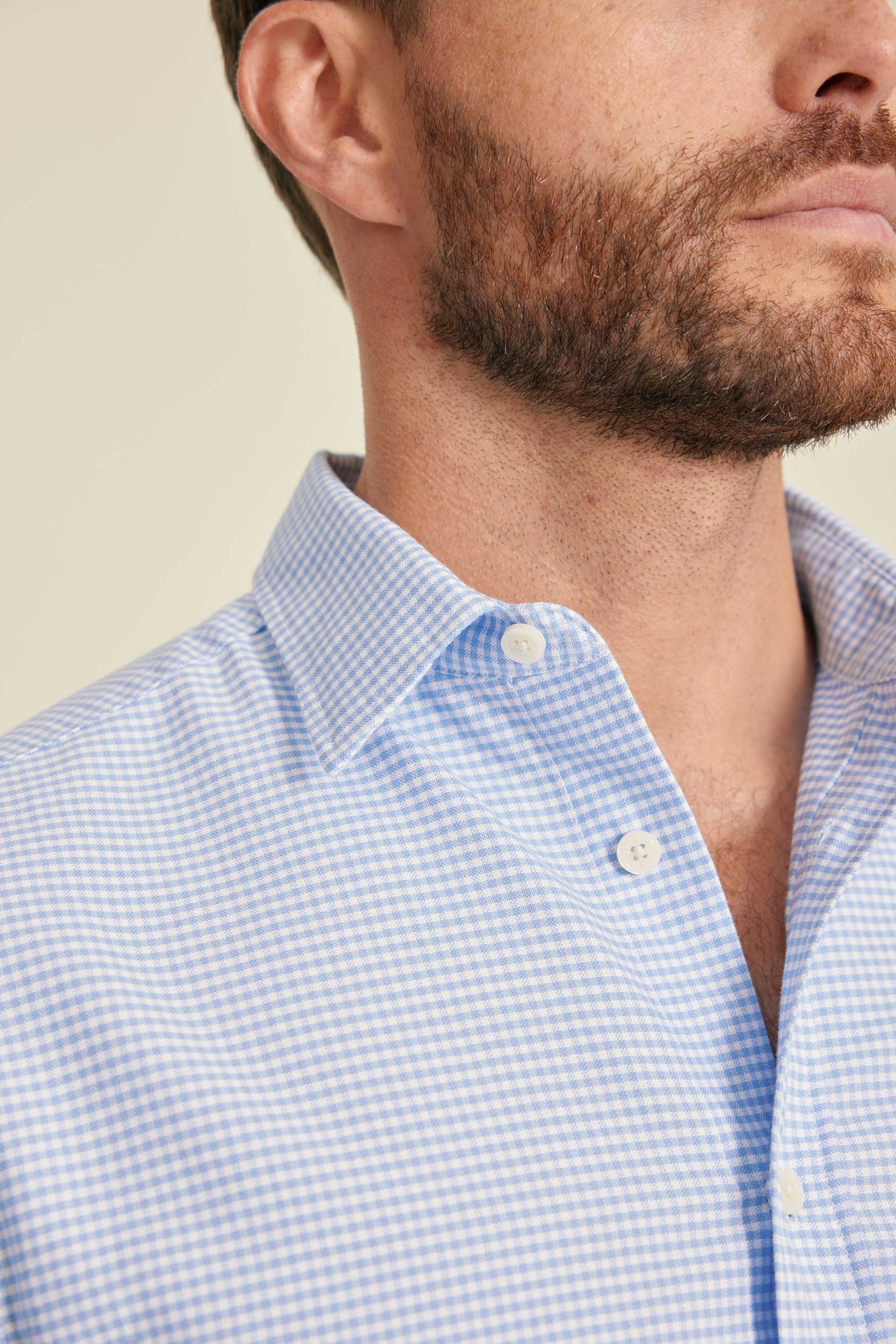 Close-up of a man wearing a light blue checkered shirt against a beige background