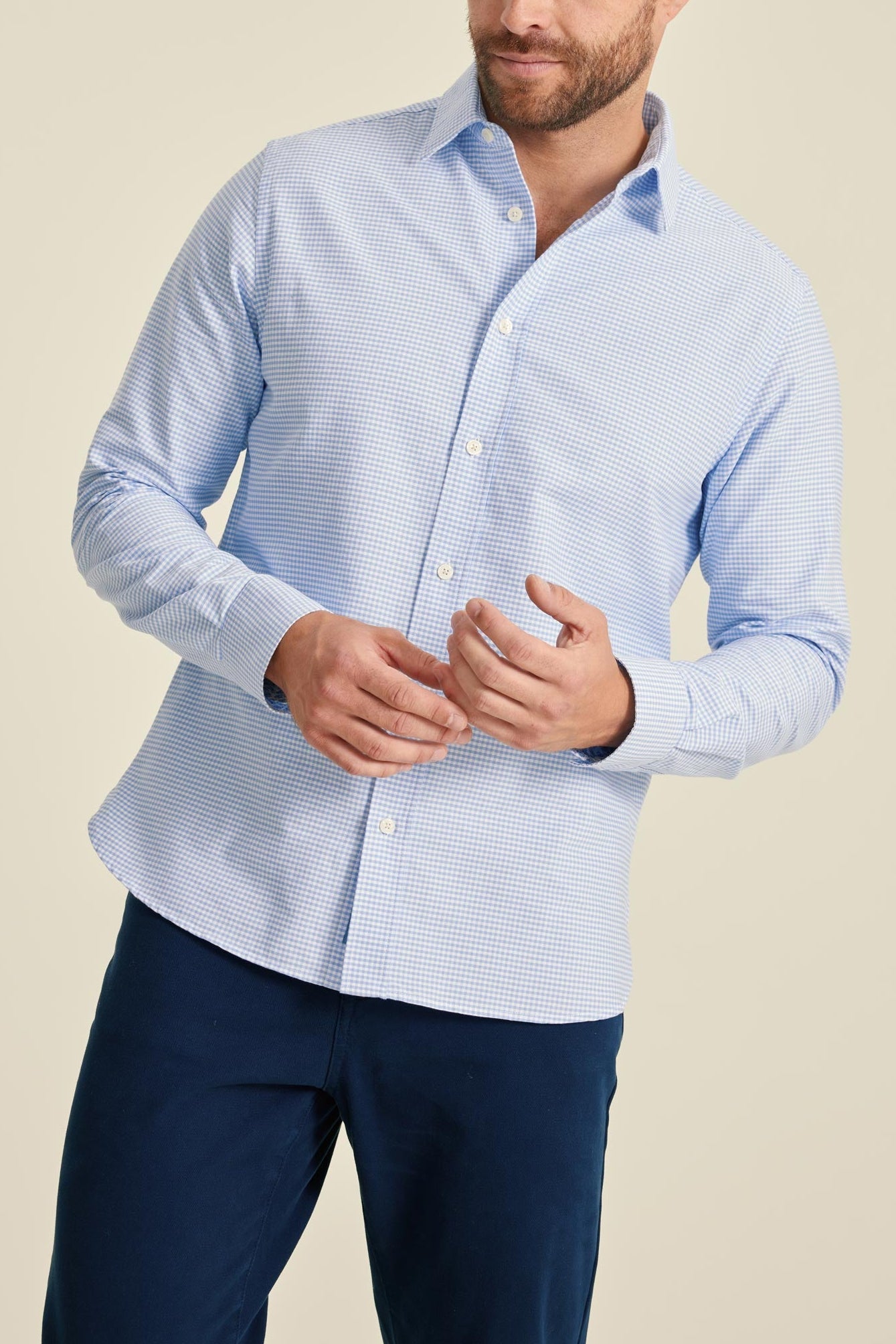 Man wearing a light blue checkered shirt and dark blue pants on a beige background