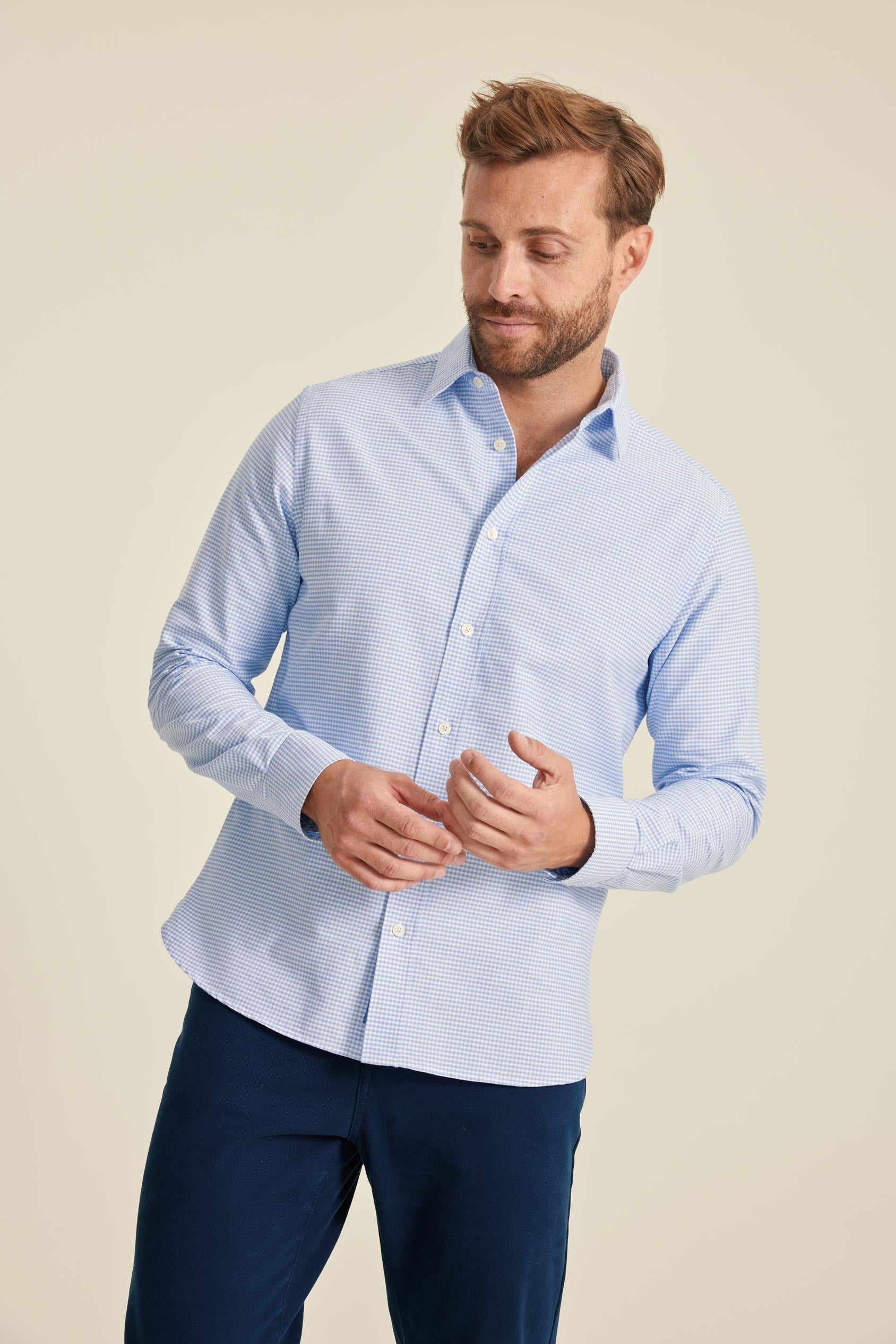 Man wearing a light blue checkered shirt and dark blue pants on a beige background