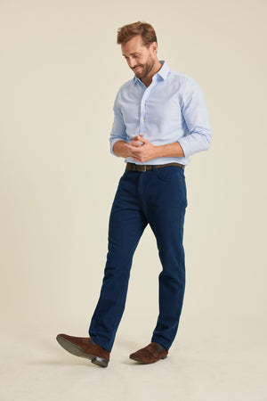 Man wearing a light blue shirt and dark blue pants on a beige background