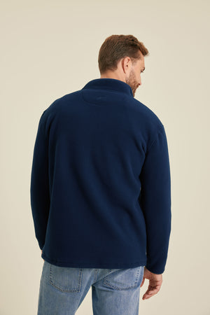 Man wearing a navy fleece jacket and blue jeans on a beige background