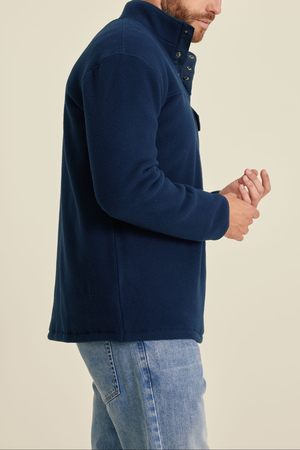 Man wearing a navy blue fleece jacket and jeans on a beige background