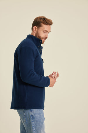 Man wearing a navy blue fleece jacket and jeans on a beige background