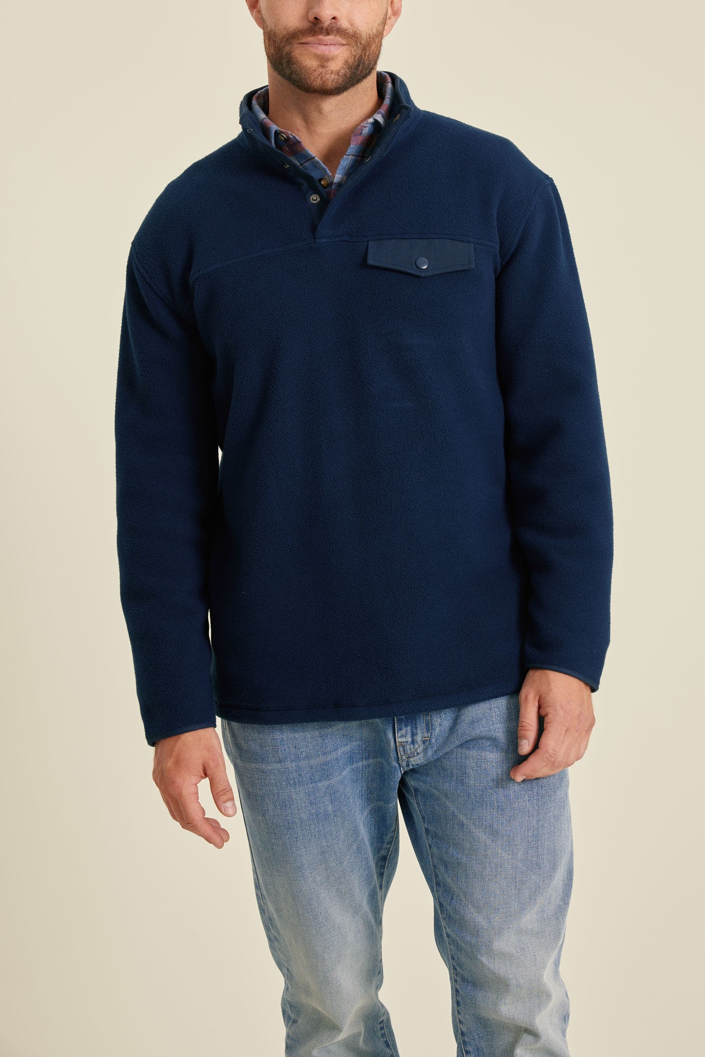Man wearing a navy fleece pullover and light blue jeans on a beige background